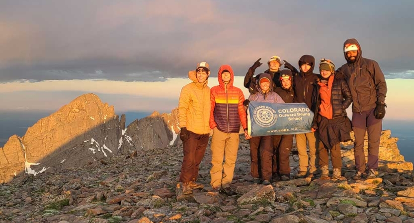 A group of people stand at the summit of a rocky mountain 